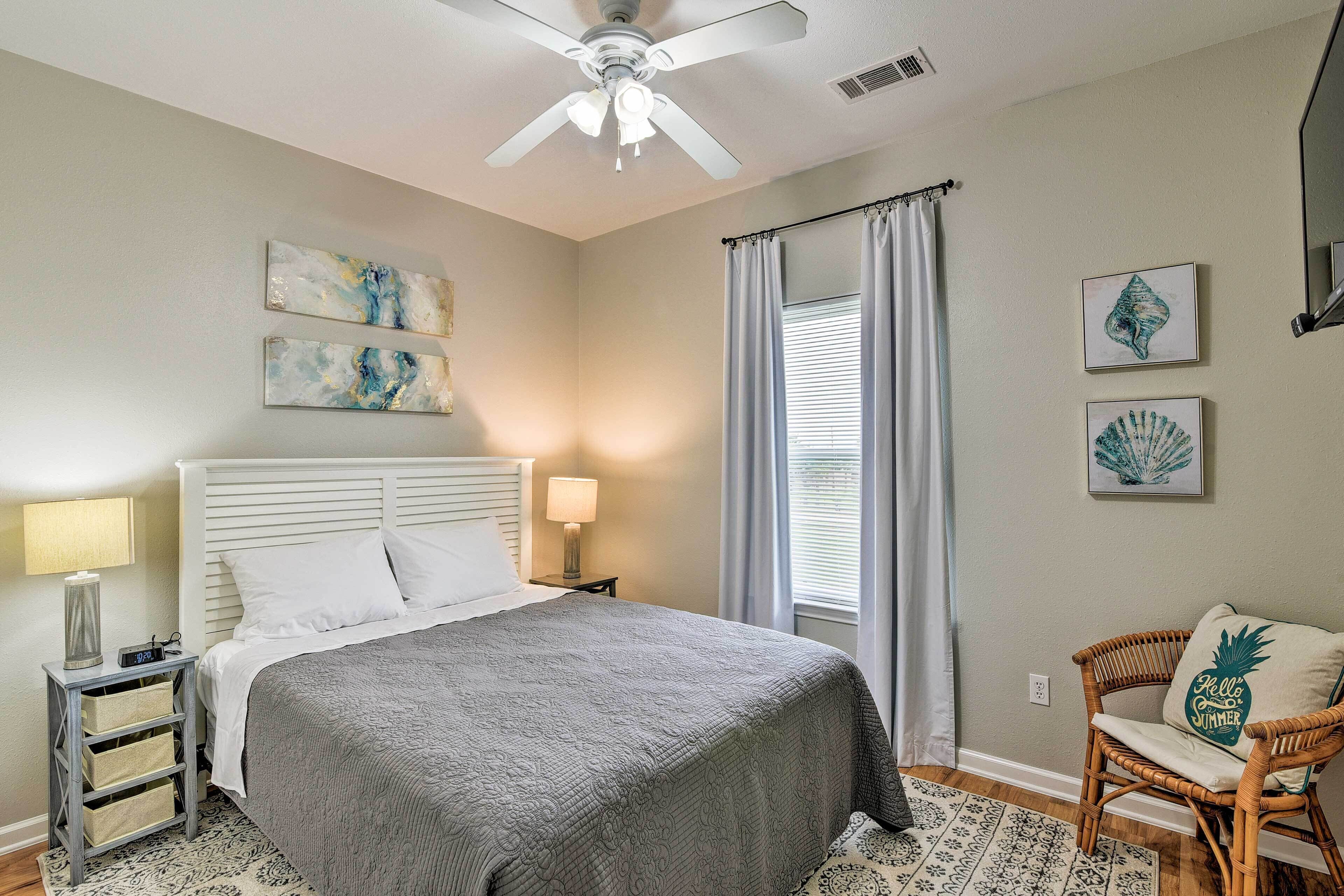 Un dormitorio con cama, mesita de noche, silla, ventilador de techo y obras de arte en las paredes.