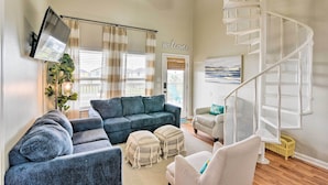 A modern living room with a blue sectional sofa, a white chair, a white spiral staircase, and a 'welcome' sign on the wall.
