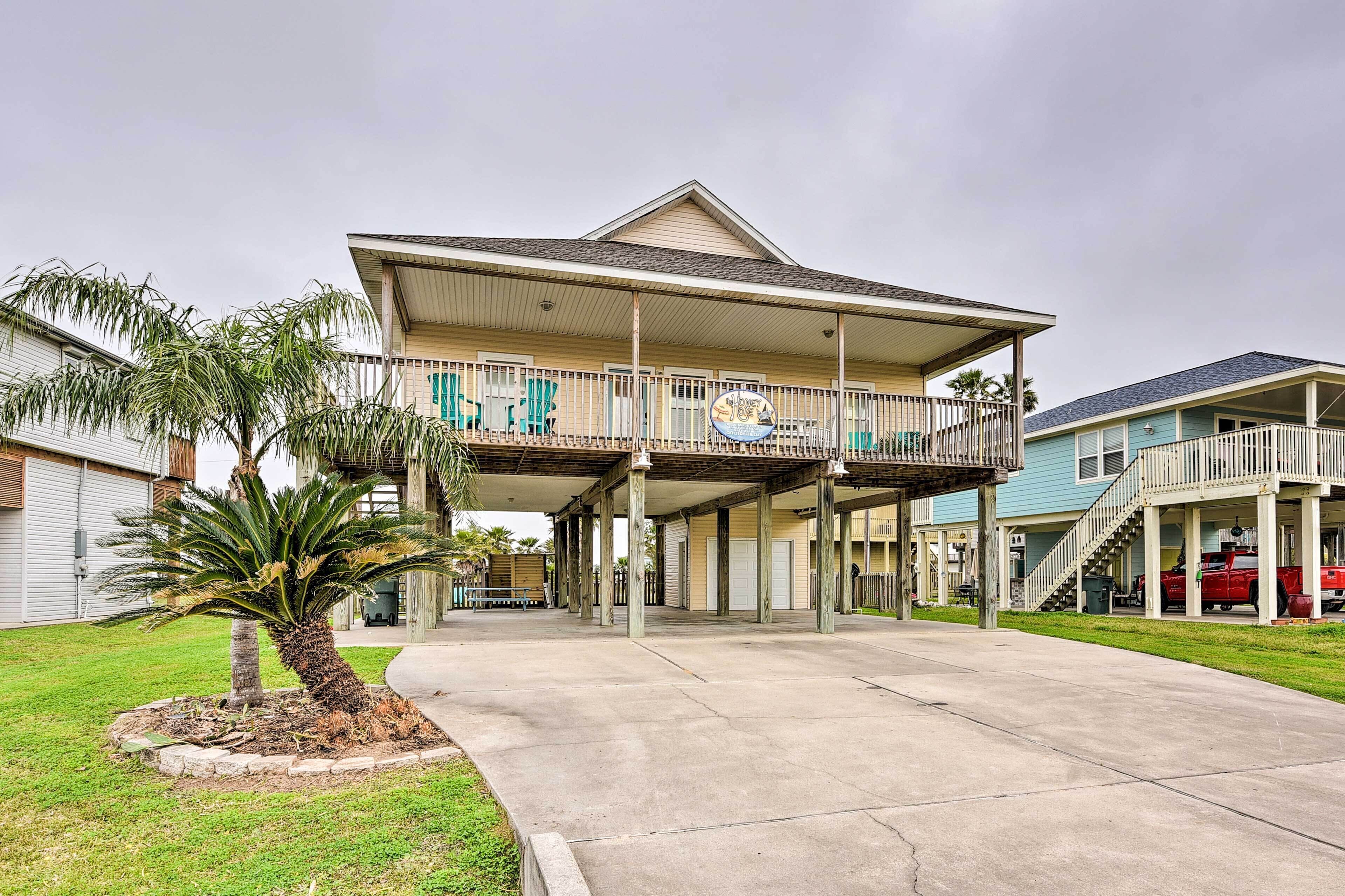 A two-story building with a balcony, a covered parking area, and a palm tree.