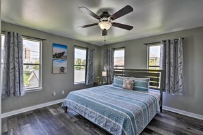 A bedroom with a bed, a ceiling fan, and two windows with curtains.
