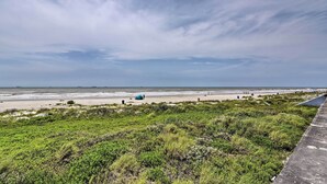 A coastal landscape with a beach, grassy dunes, and a clear sky.