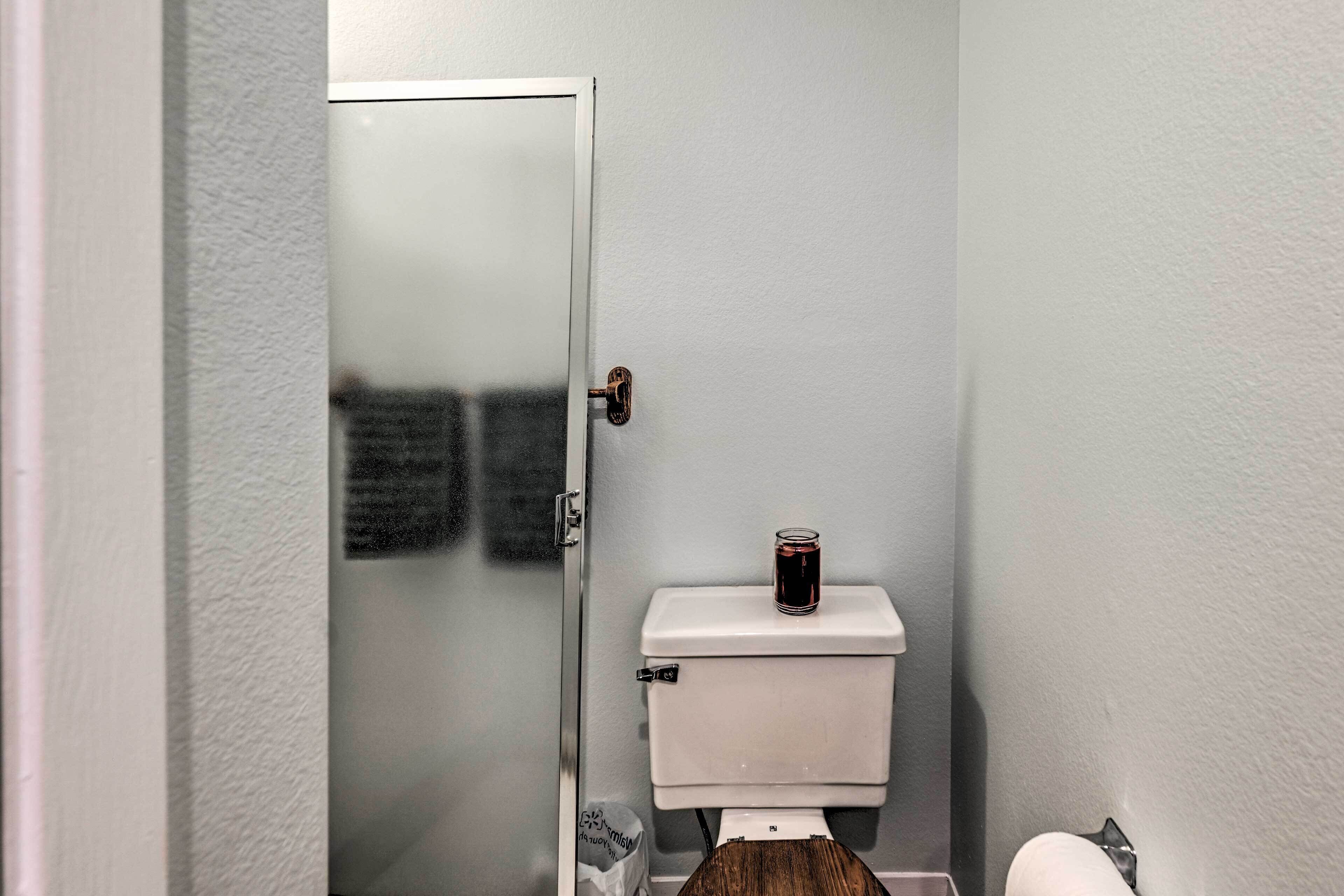 Un baño con inodoro blanco, cabina de ducha de vidrio y un pequeño recipiente de vidrio sobre el tanque del inodoro.