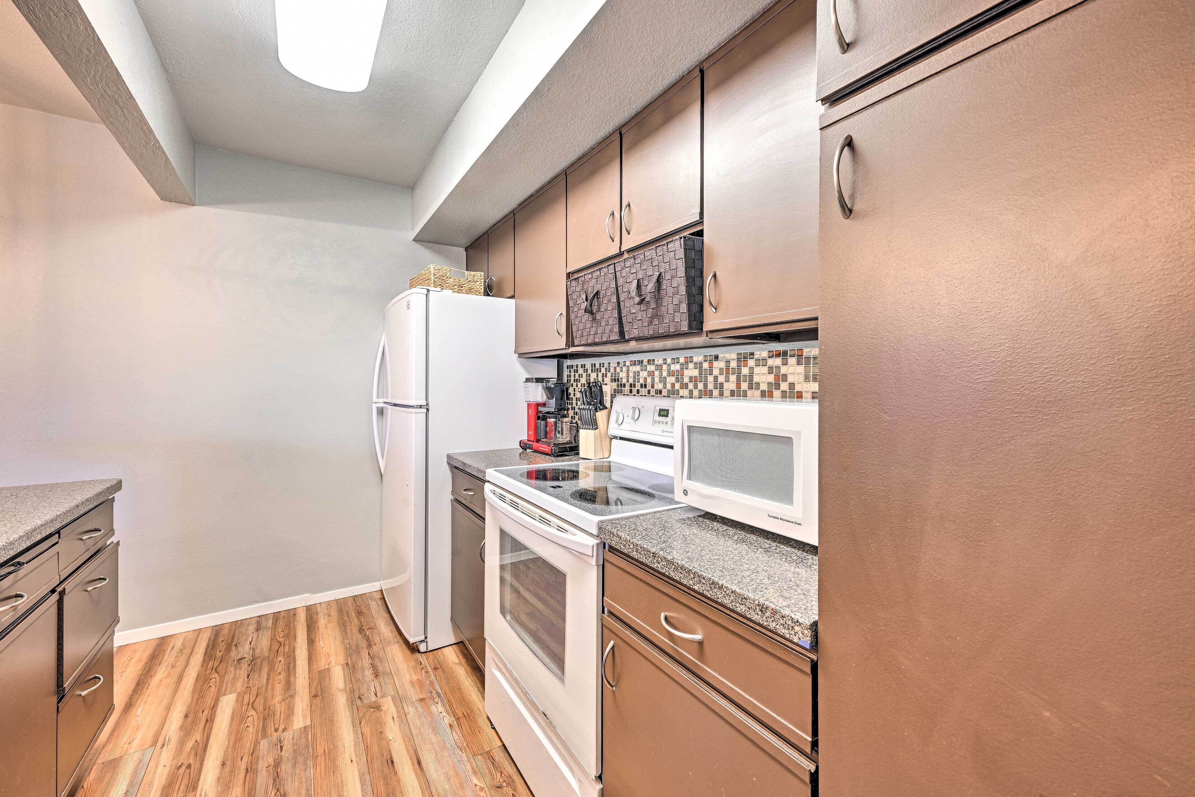 A kitchen with wooden flooring, a refrigerator, a microwave, and cabinets.