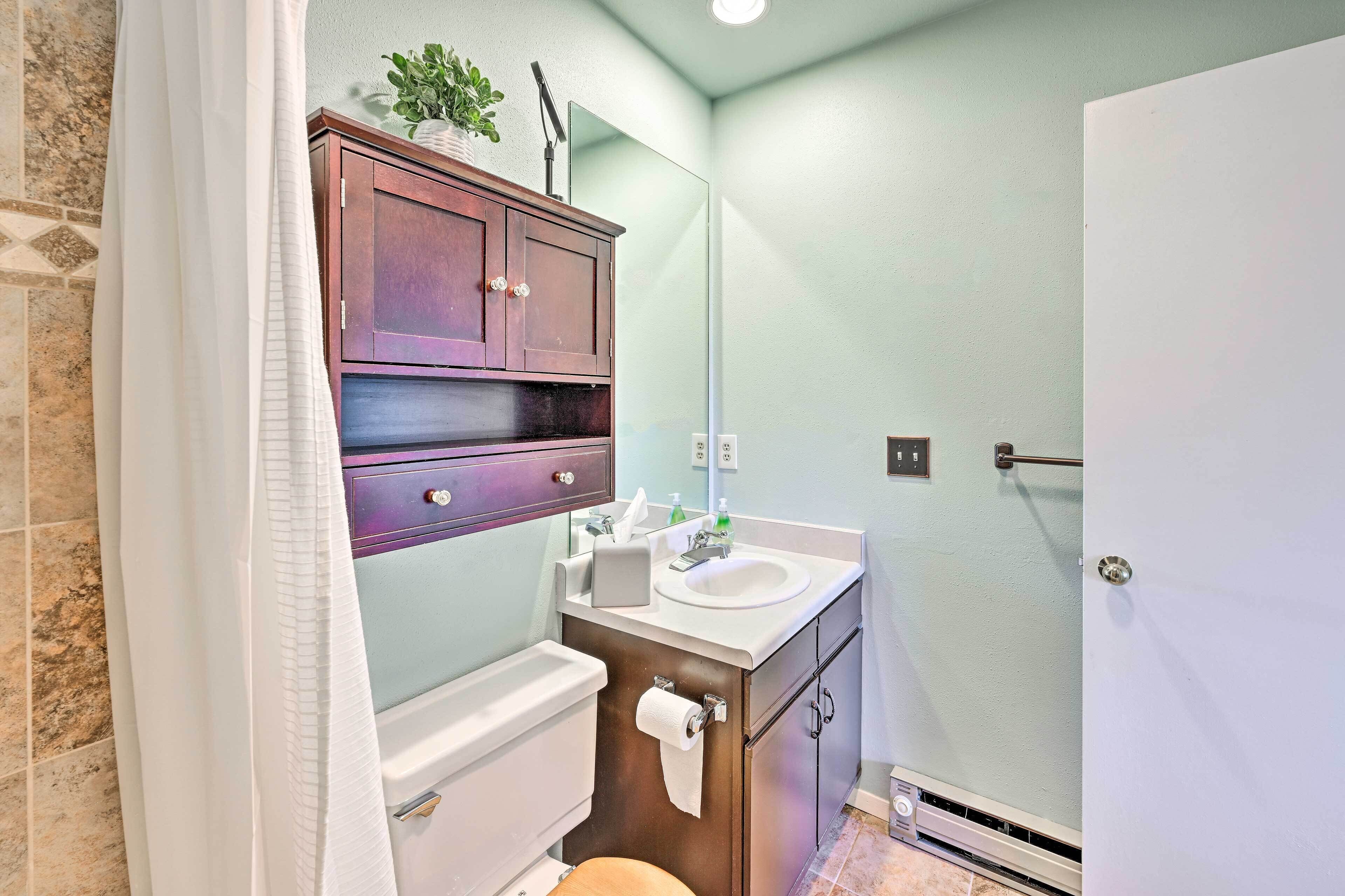 A bathroom with a toilet, sink, cabinet, and a shower area.