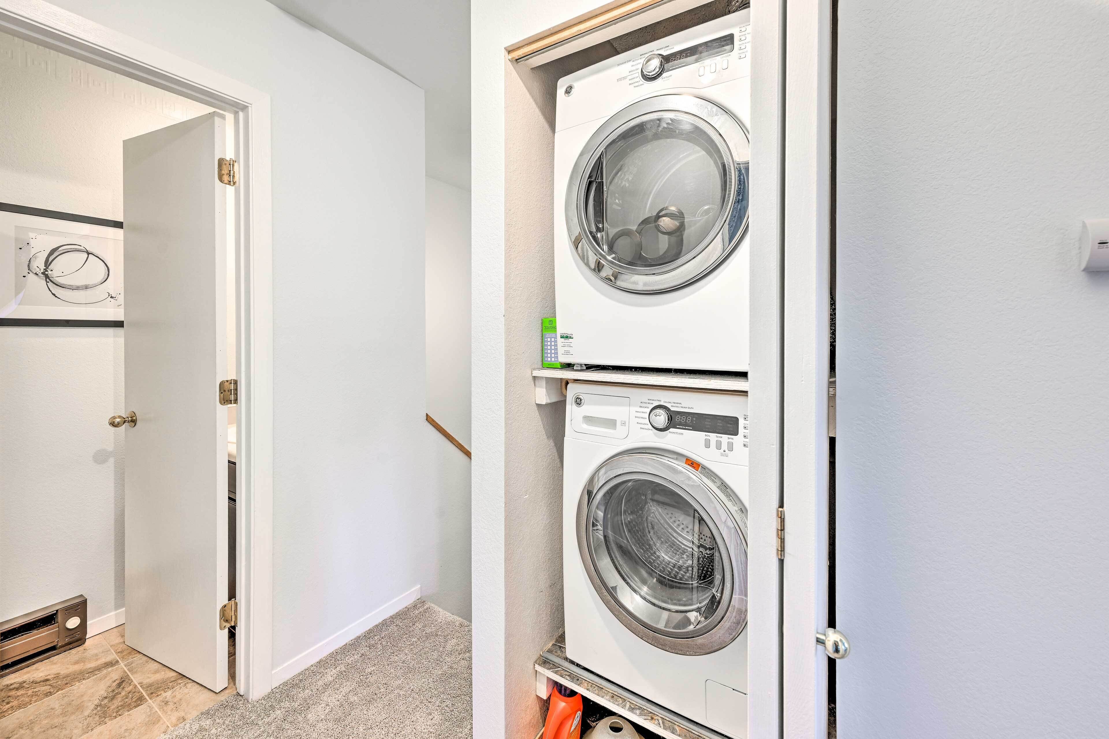 A laundry room with two stacked front-loading washing machines, a door with a brass handle, and a wall-mounted thermostat.