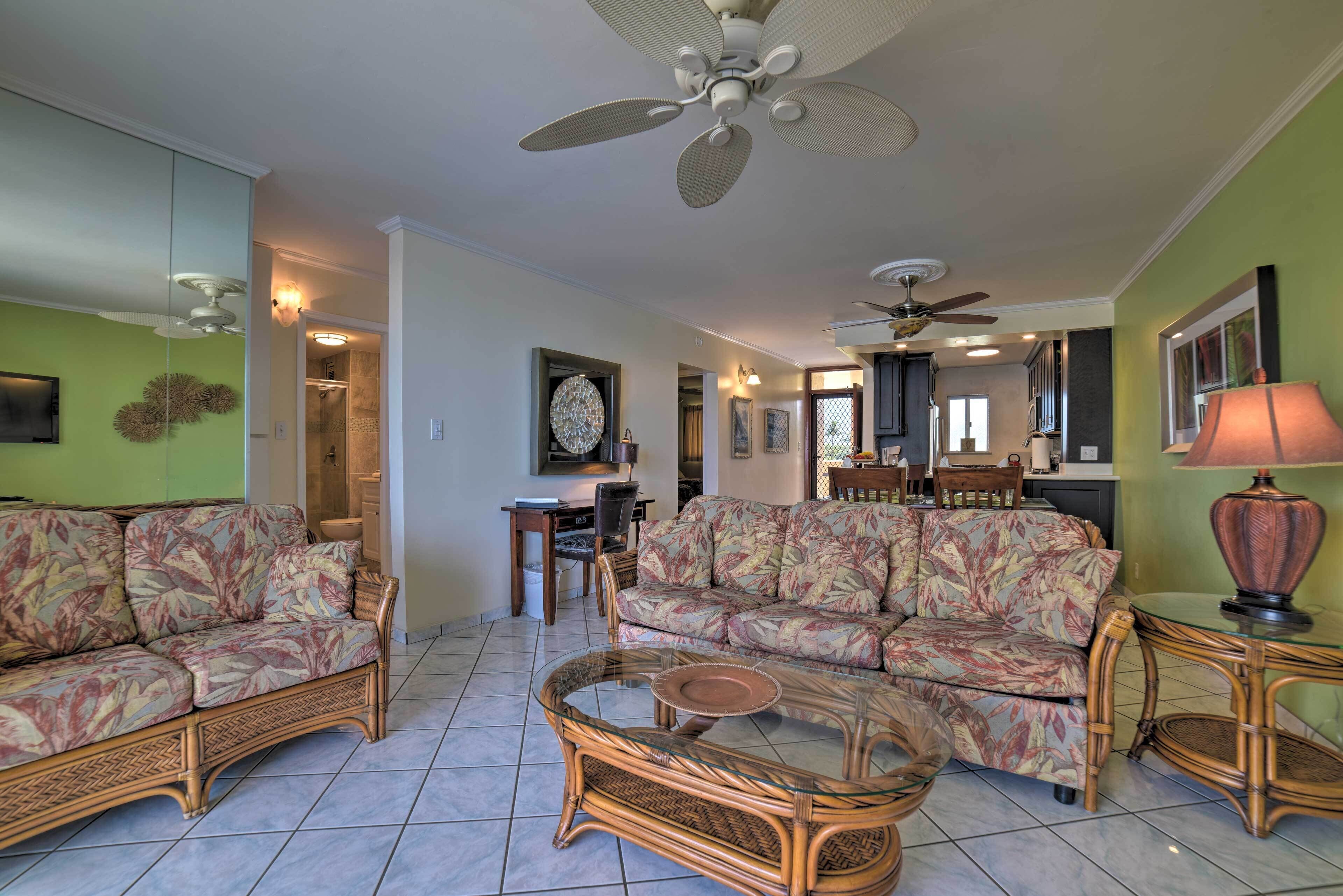 A living room with two sofas, a glass coffee table, and a ceiling fan.