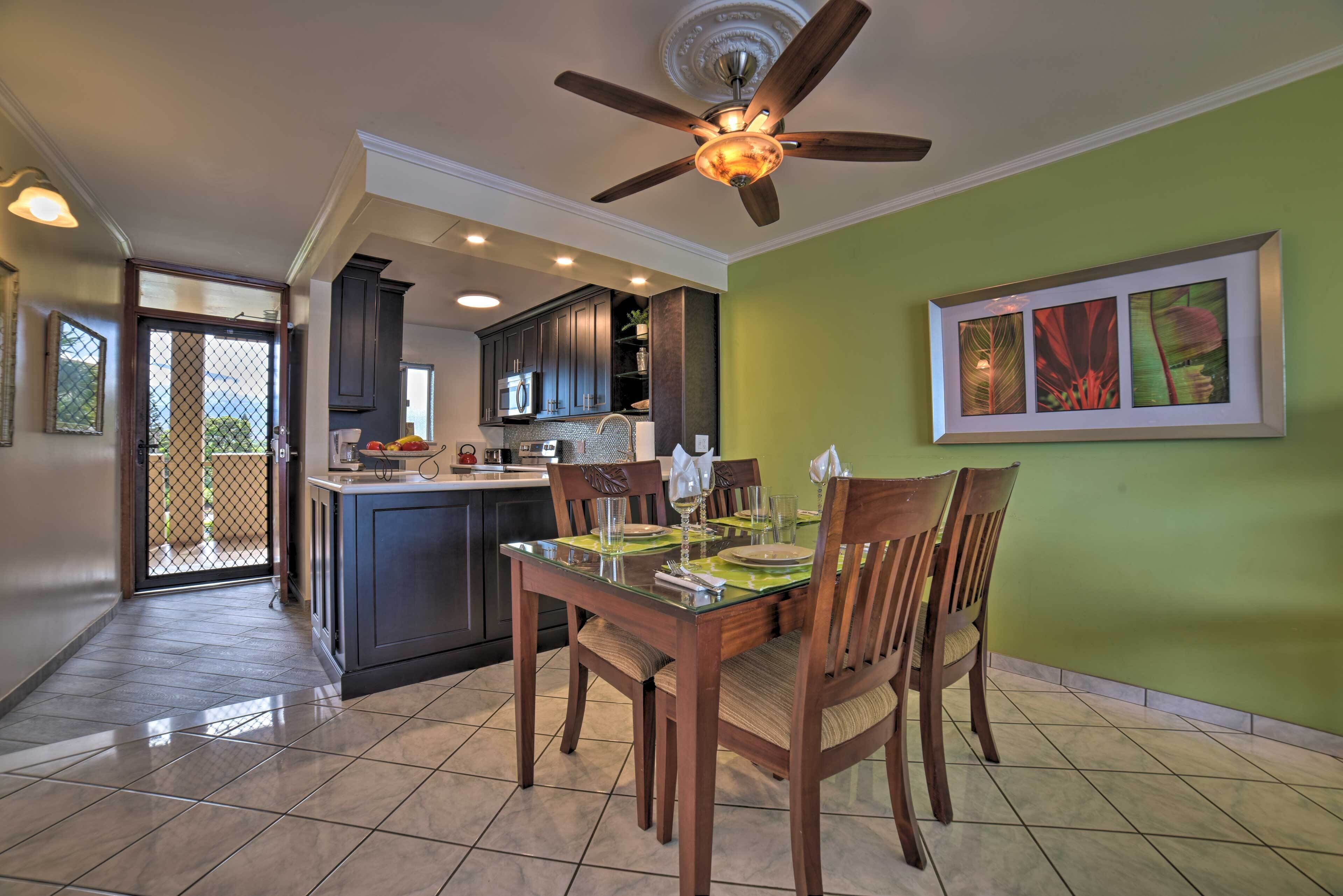A dining area with a glass table, wooden chairs, and a ceiling fan.