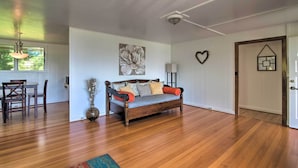 A spacious room with a wooden floor, a sofa with cushions, a dining table with chairs, and a decorative vase. - Hilo Apartment: Ocean Views on the Hamakua Coast! (Hilo)