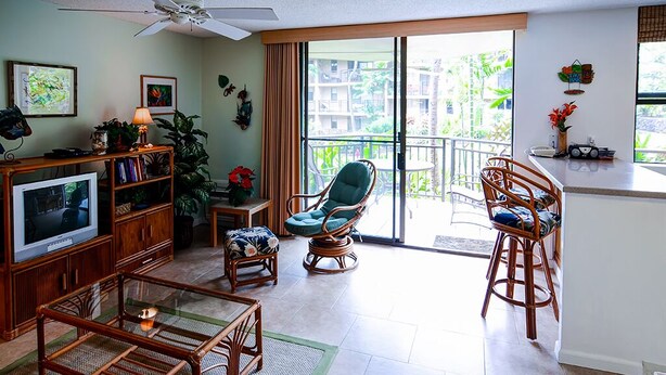 A living room with a TV, bookshelves, a glass coffee table, and wicker chairs. - Oceanview Kailua-kona Condo With Private Balcony! (Kailua-Kona)