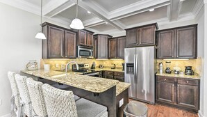 A kitchen with dark wood cabinets, stainless steel appliances, a granite countertop, and a woven chair. - Half-mi to Inlet Beach: Home w/ Grill & Fire Pit (Panama City Beach)