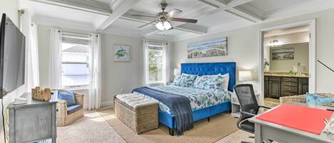A bedroom with a large bed, a desk, a chair, a ceiling fan, and a window with curtains.