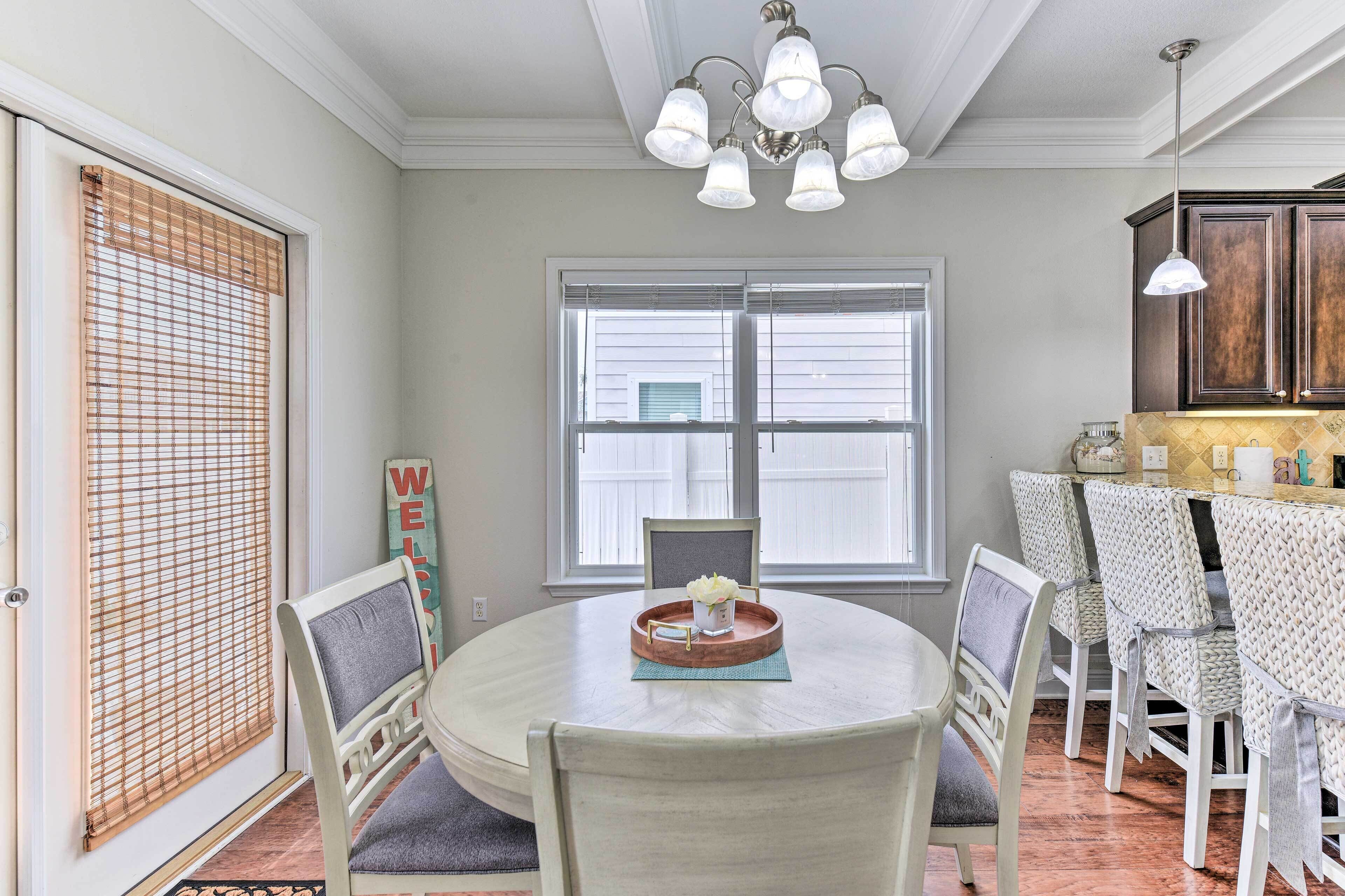 A dining area with a round table, chairs, a chandelier, and a view of the outside through large windows.