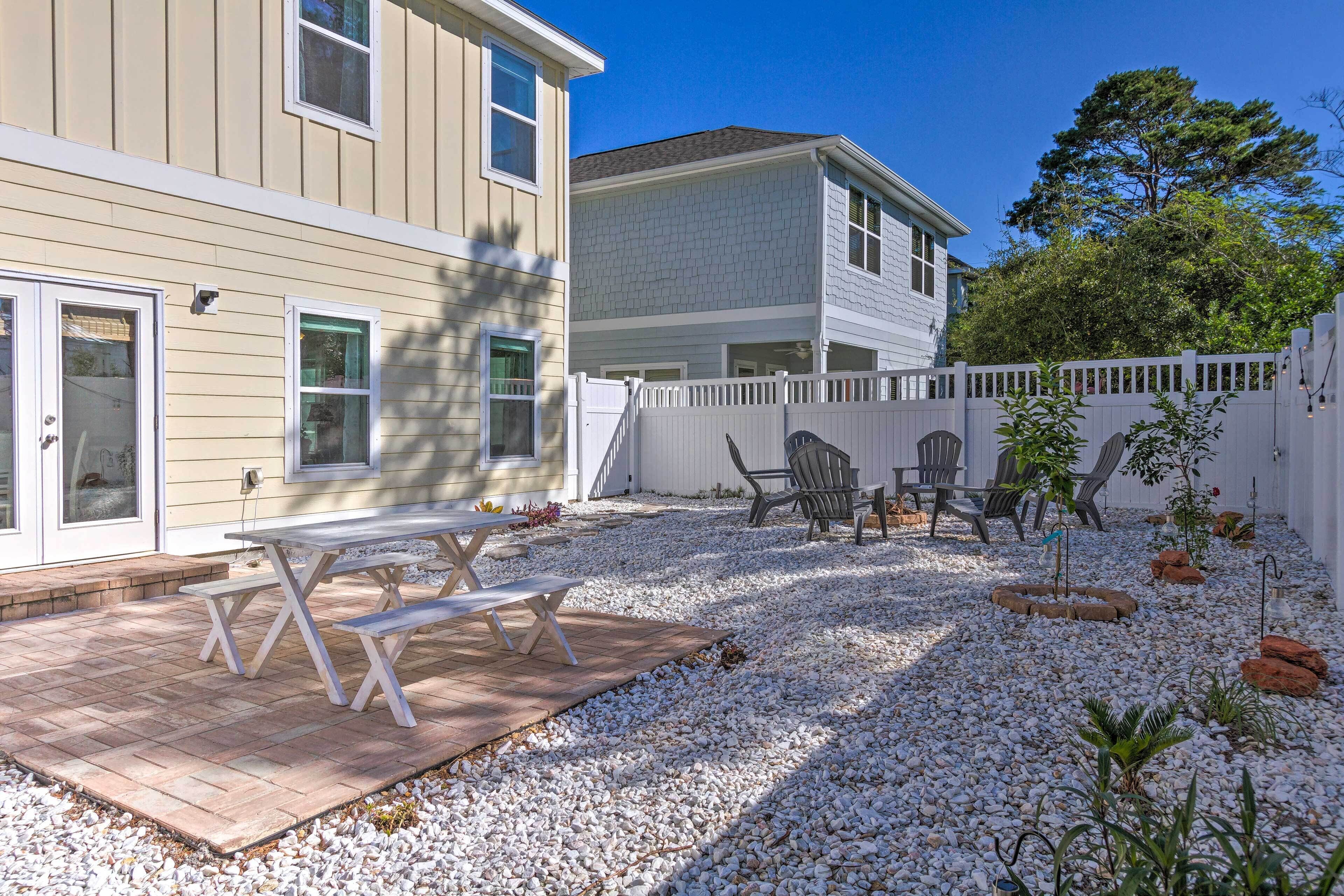 A patio with a picnic table and chairs, surrounded by a white fence and gravel.