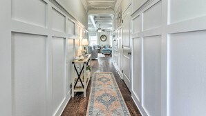 A hallway with white paneled walls, a patterned rug, a ceiling fan, and a round mirror on the wall. - Half-mi to Inlet Beach: Home w/ Grill & Fire Pit (Panama City Beach)