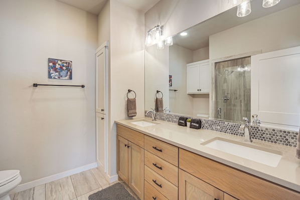 A bathroom with a double sink vanity, a large mirror, and a shower area.