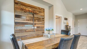 Un comedor con una mesa y sillas de madera, una obra de arte rústica en la pared y una planta pequeña en una mesita auxiliar.