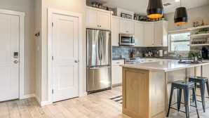 Una cocina moderna con armarios blancos, electrodomésticos de acero inoxidable, una isla de madera y taburetes negros.