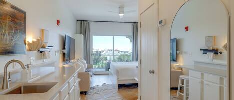 A modern hotel room with a kitchen, a large window, a bed, and a bathroom.