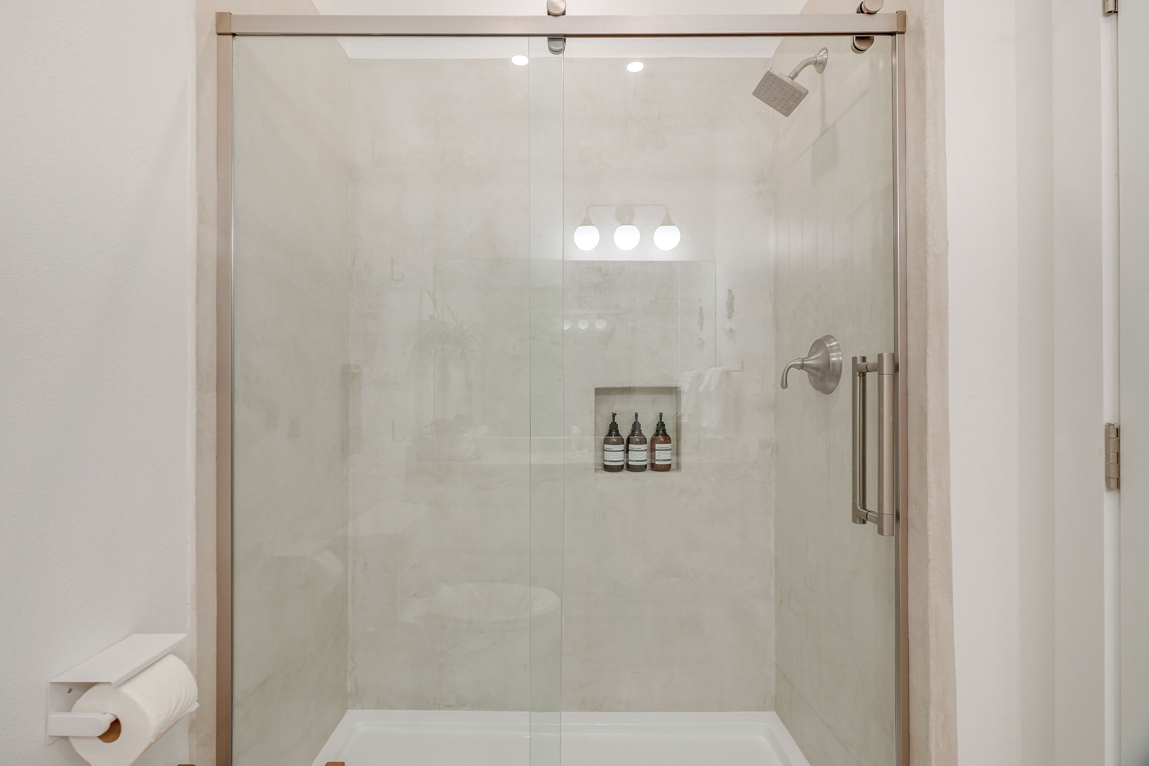 A modern bathroom with a glass-enclosed shower, a toilet paper holder, and a shelf with toiletries.