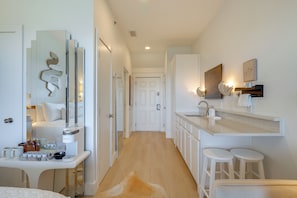 A modern hotel room with a large mirror, a white vanity, a sink, and a small seating area.