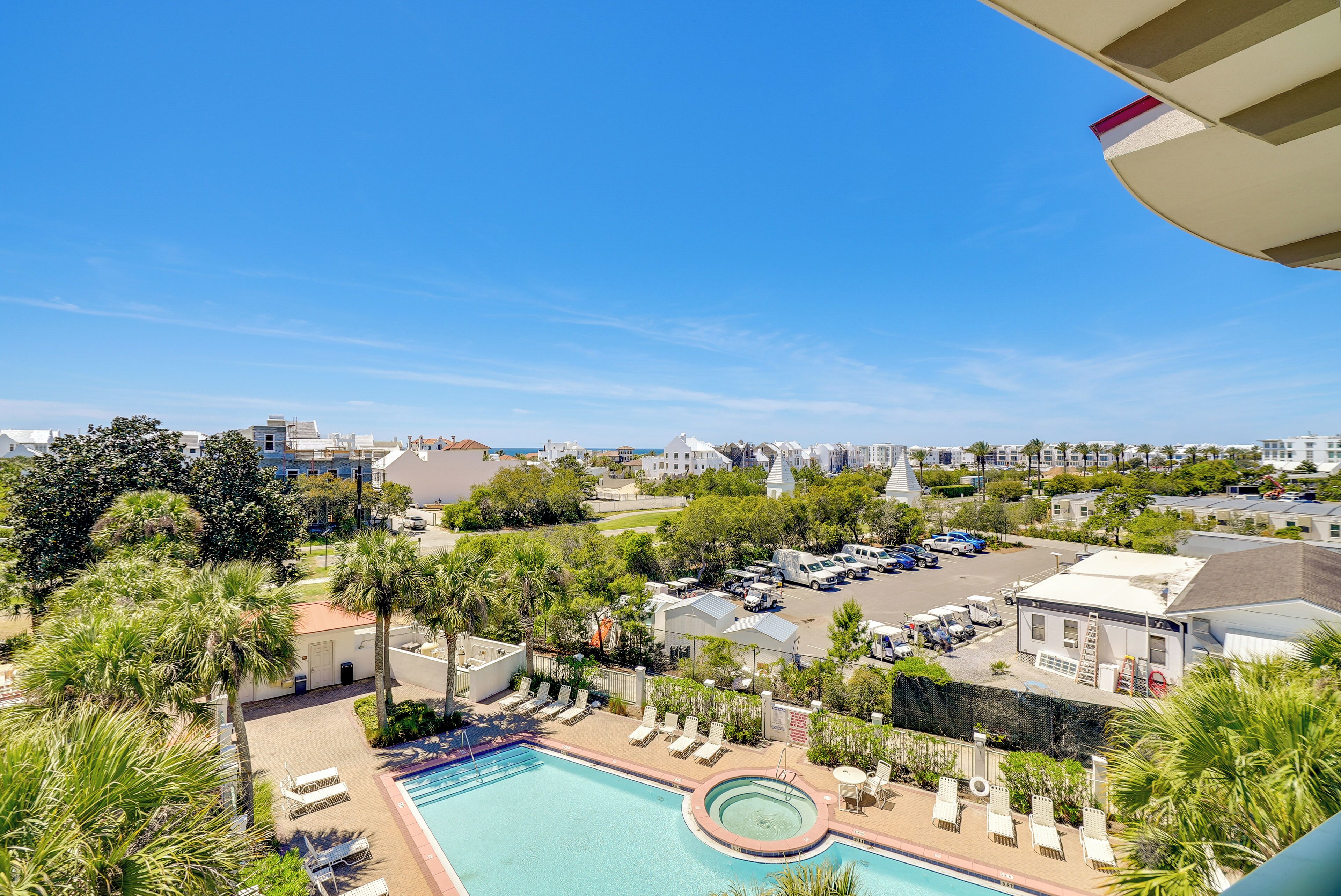 A pool area with lounge chairs, a circular hot tub, and a view of a parking lot with vehicles.