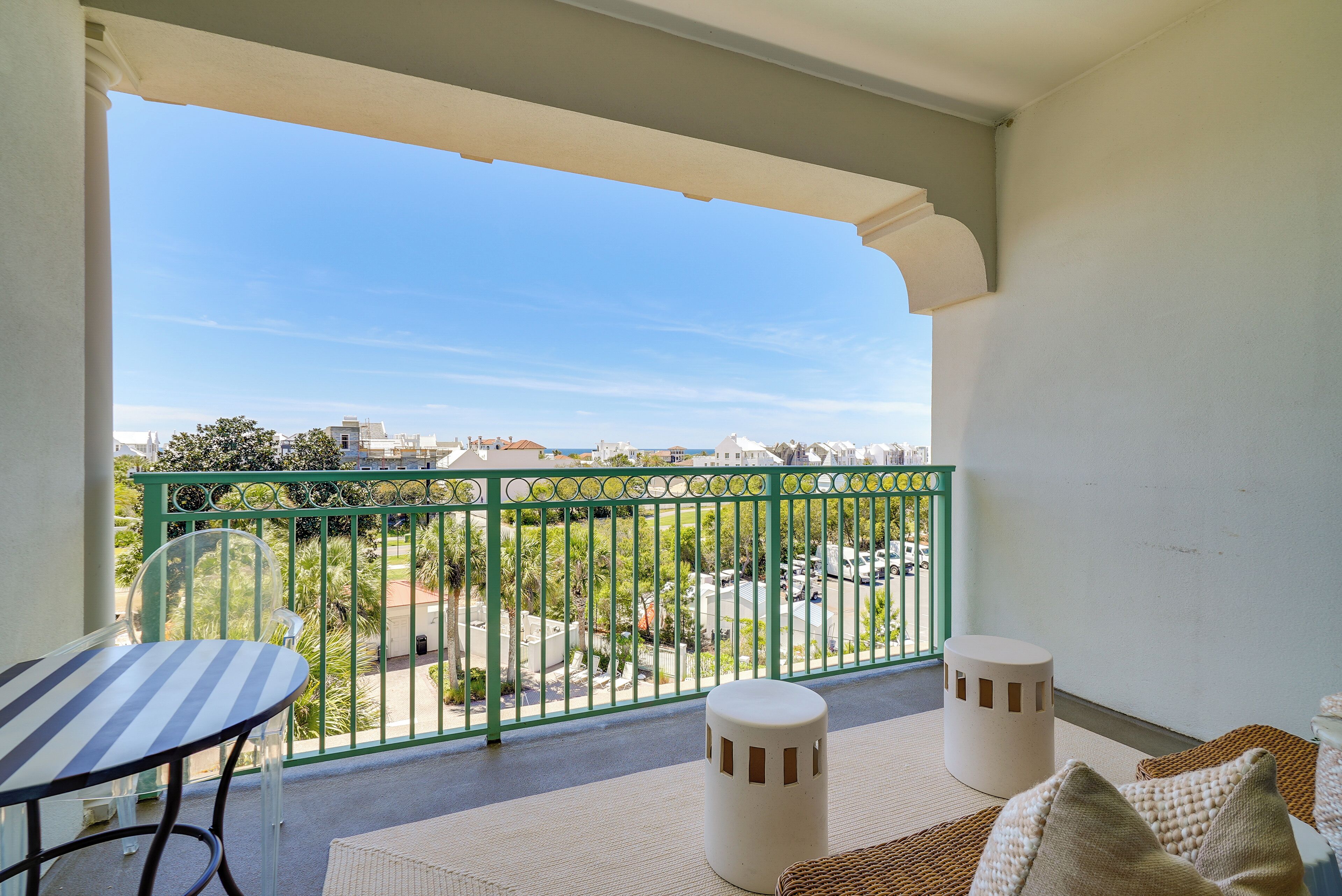 A balcony with a view of a cityscape, a table, and two ottomans.