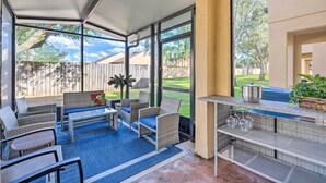 Ein überdachter Patio-Bereich mit Korbmöbeln, einem Tisch und einer Grillstation.