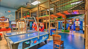 Ein mehrstöckiger Indoor-Spielbereich mit verschiedenen Spielautomaten, einem Tischtennis-Tisch und einem Holzstuhl.
