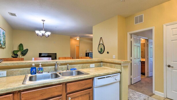 A kitchen with wooden cabinets, a dishwasher, a double sink, and a ceiling light. - Sun-soaked Kissimmee Gem w/ Resort Amenities! (Kissimmee)