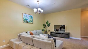 A living room with a sectional sofa, a flat-screen TV, a plant, and a painting on the wall. - Sun-soaked Kissimmee Gem w/ Resort Amenities! (Kissimmee)