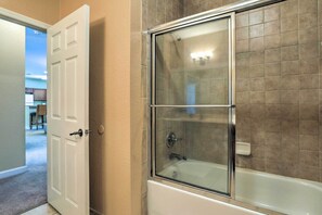 A bathroom with a glass-enclosed shower, a white bathtub, and beige tiled walls. - Sun-soaked Kissimmee Gem w/ Resort Amenities! (Kissimmee)