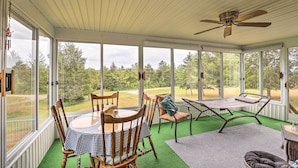 Un patio techado con mesa y sillas, un ventilador de techo y ventanas amplias con vistas al exterior.