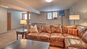A living room with a brown leather couch, a coffee table, a lamp, a basketball hoop, and a window with a view of trees. - 2 Mi to Slopes! Hot Tub Hideaway in Breckenridge (Breckenridge)