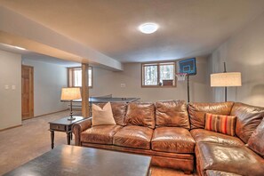 A living room with a brown leather couch, a coffee table, a lamp, a basketball hoop, and a window with a view of trees. - 2 Mi to Slopes! Hot Tub Hideaway in Breckenridge (Breckenridge)