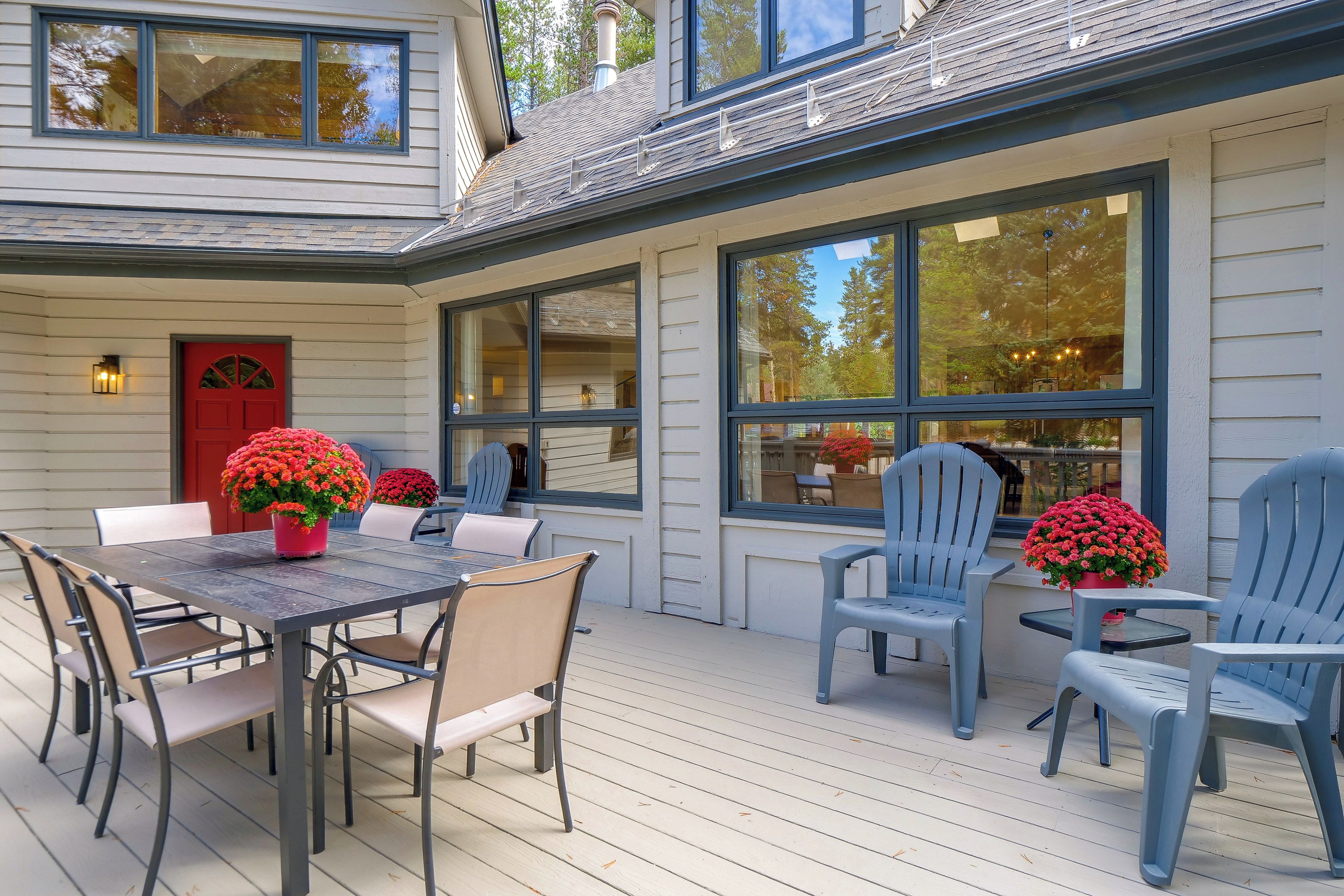 A covered patio with a dining table and chairs, large windows, and a red door.
