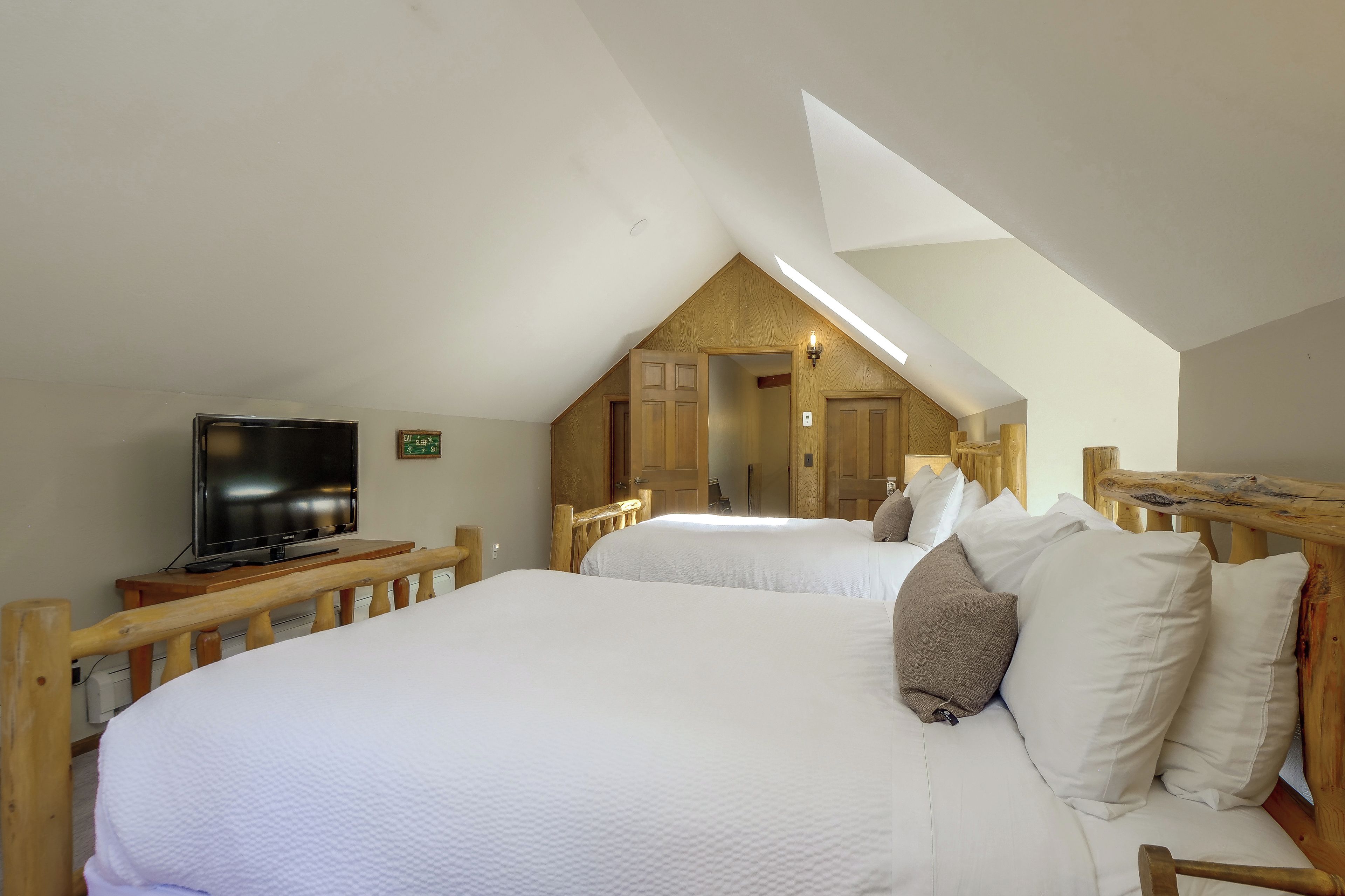 A bedroom with two beds, a television, and a wooden headboard.
