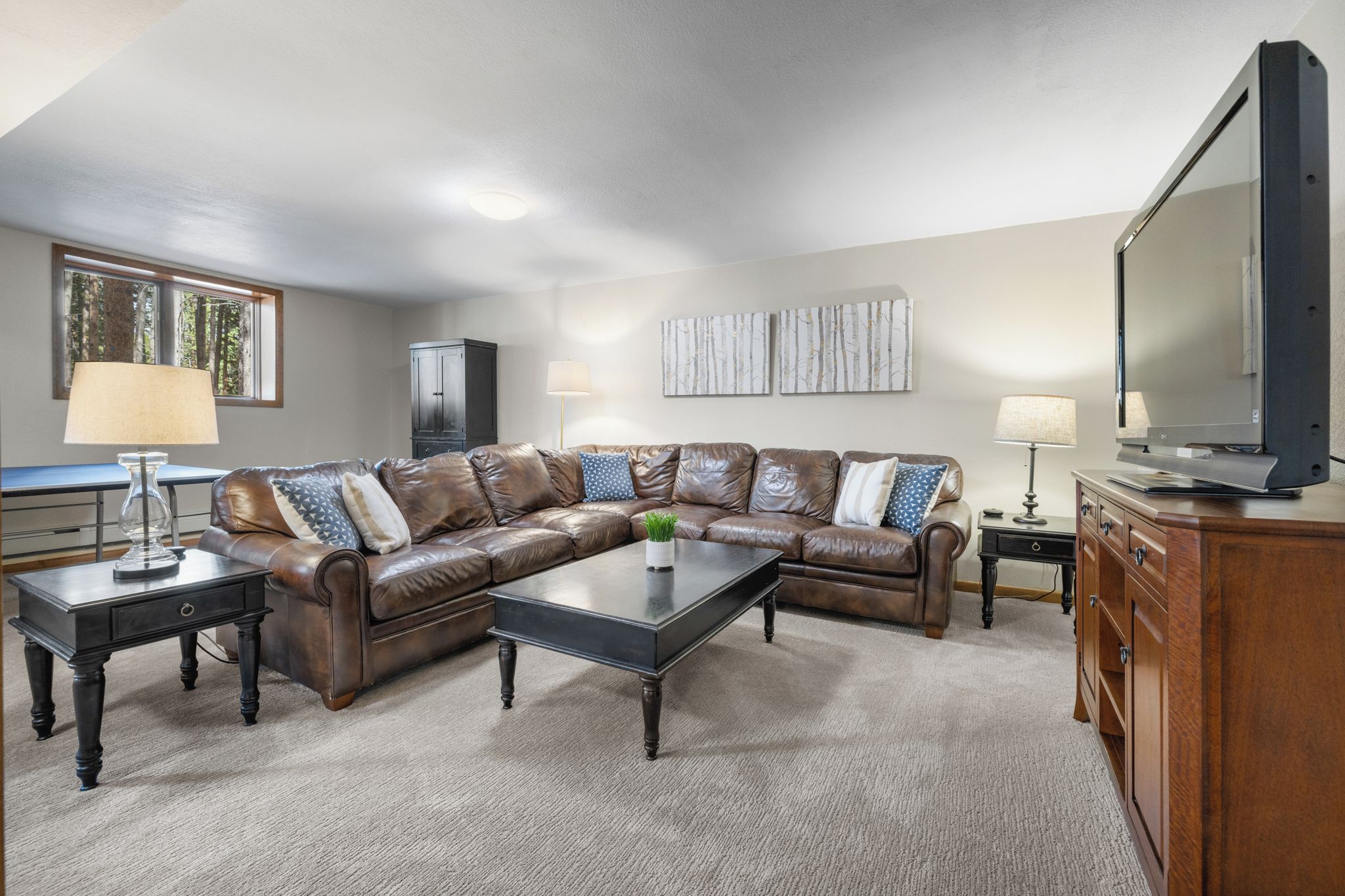 A living room with a L-shaped sectional sofa, a coffee table, a television, and a cabinet.