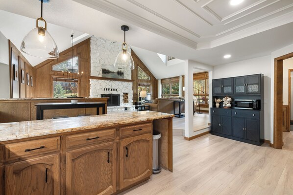 A spacious kitchen with a large island, wooden cabinets, and a stone fireplace.