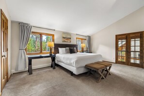 Une chambre à coucher avec un lit, des tables de chevet, un banc et de grandes fenêtres.
