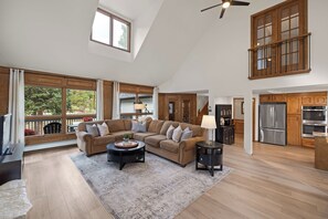 A spacious living room with a sectional sofa, a coffee table, and a view of the outdoors through large windows.