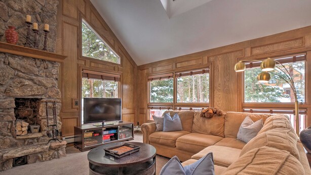 A cozy living room with a stone fireplace, large windows, a comfortable sofa, and a television.