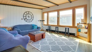 Un salon avec un canapé bleu, une table basse en bois, une grande horloge murale et une fenêtre donnant sur des immeubles.