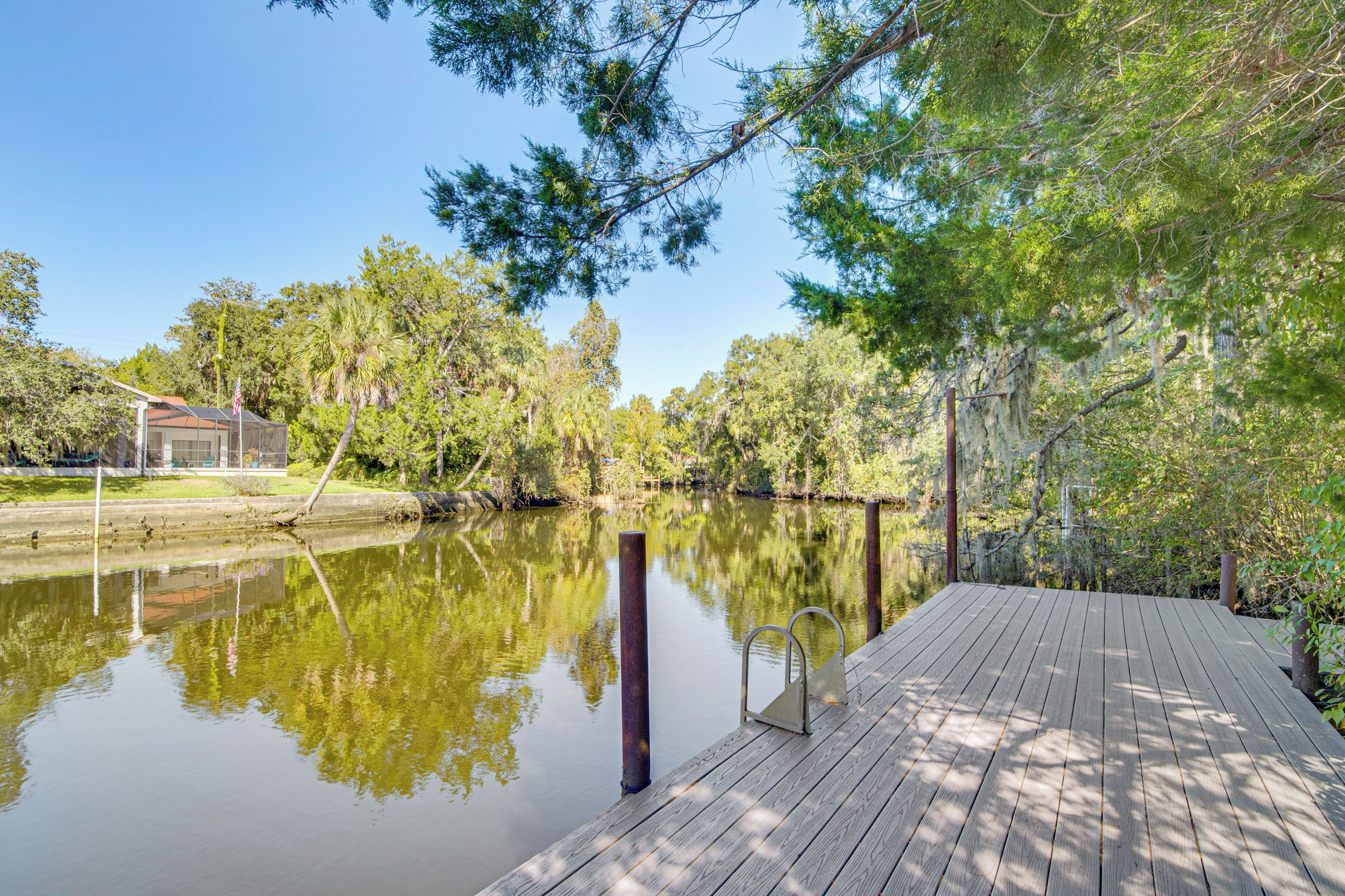A wooden dock extending over a calm river, surrounded by lush greenery and trees.