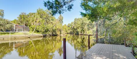 A wooden dock extending over a calm river, surrounded by lush greenery and trees.