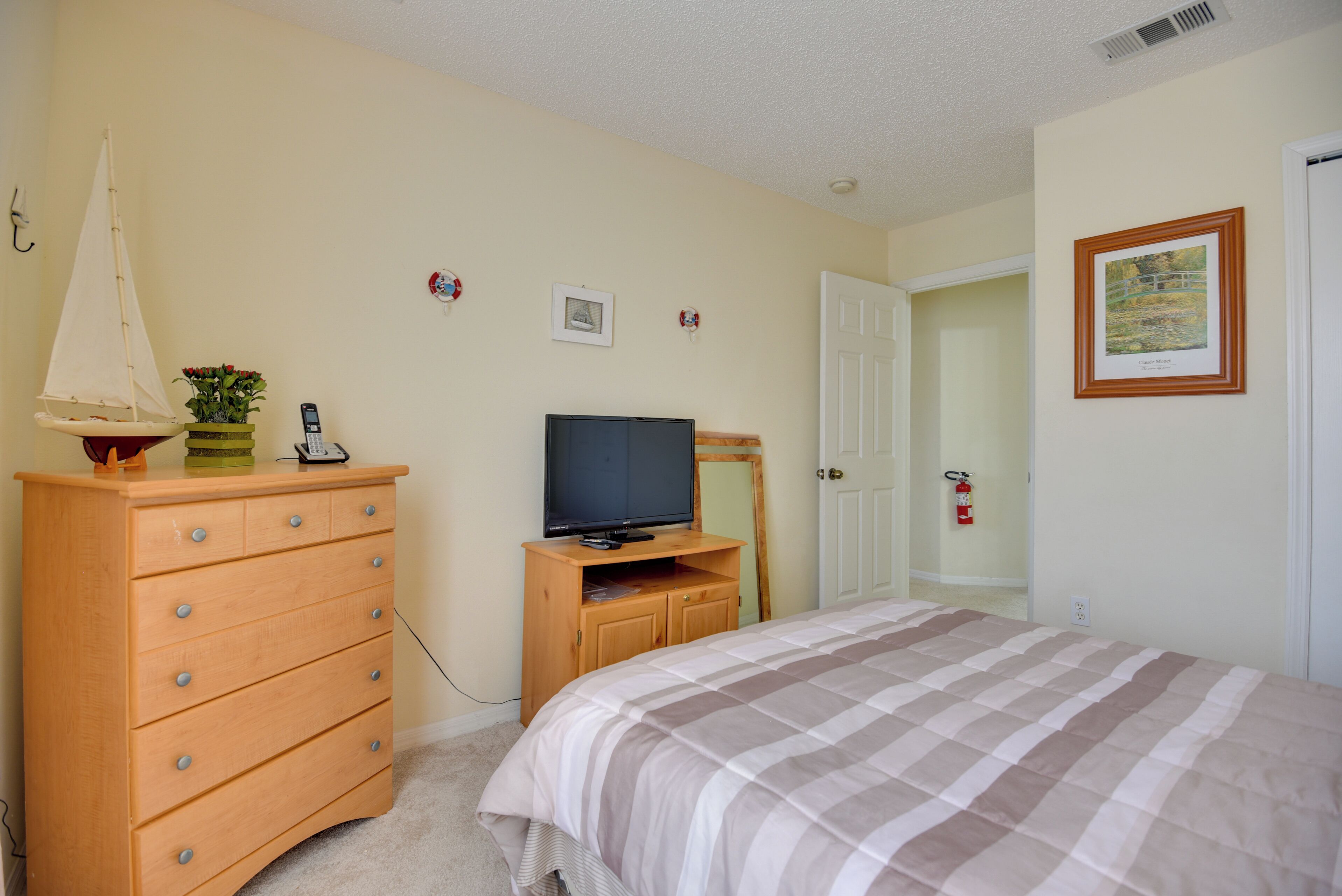 A bedroom with a bed, dresser, television, and a door leading to another room.