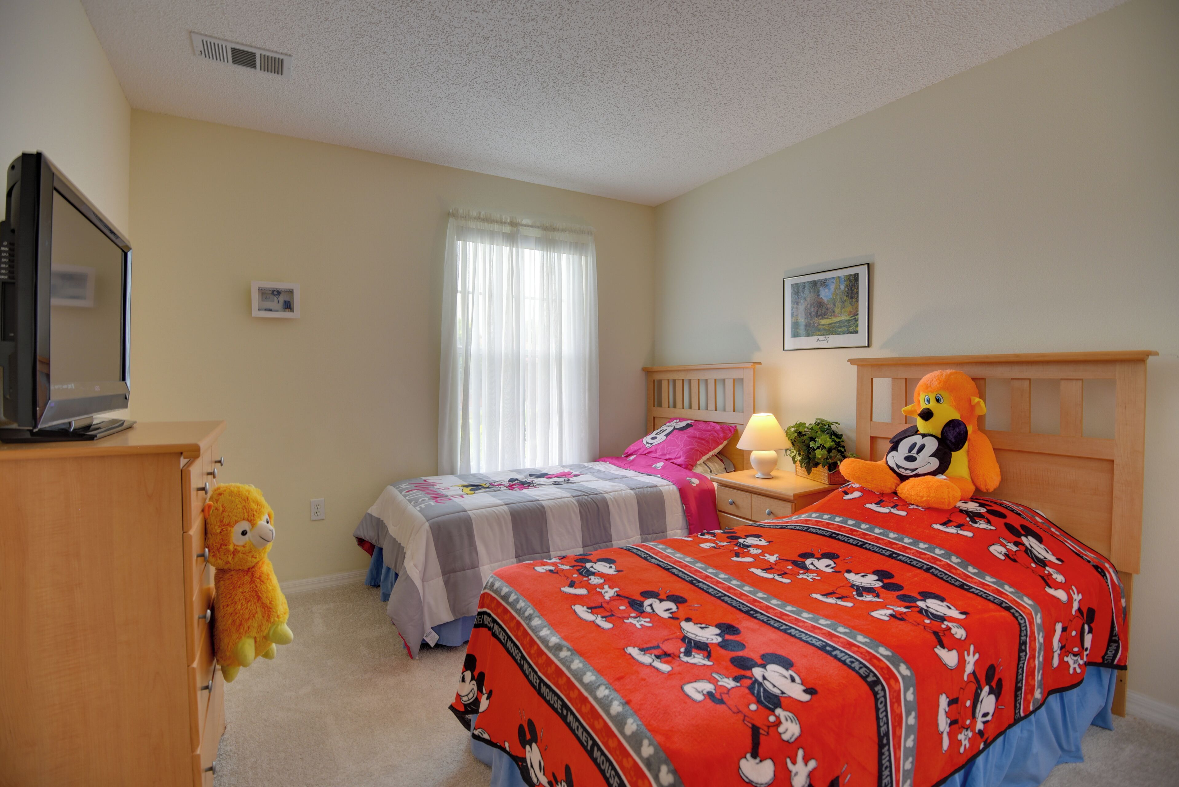 Une chambre avec deux lits, un téléviseur posé sur une commode et des peluches.