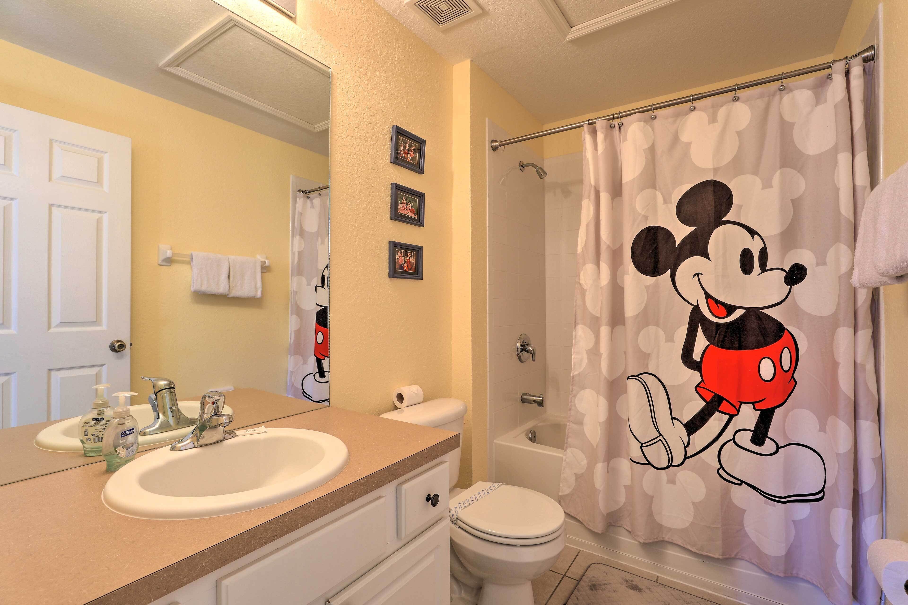 Un baño con cortina de ducha de Mickey Mouse, un lavamanos, un inodoro y un espejo.