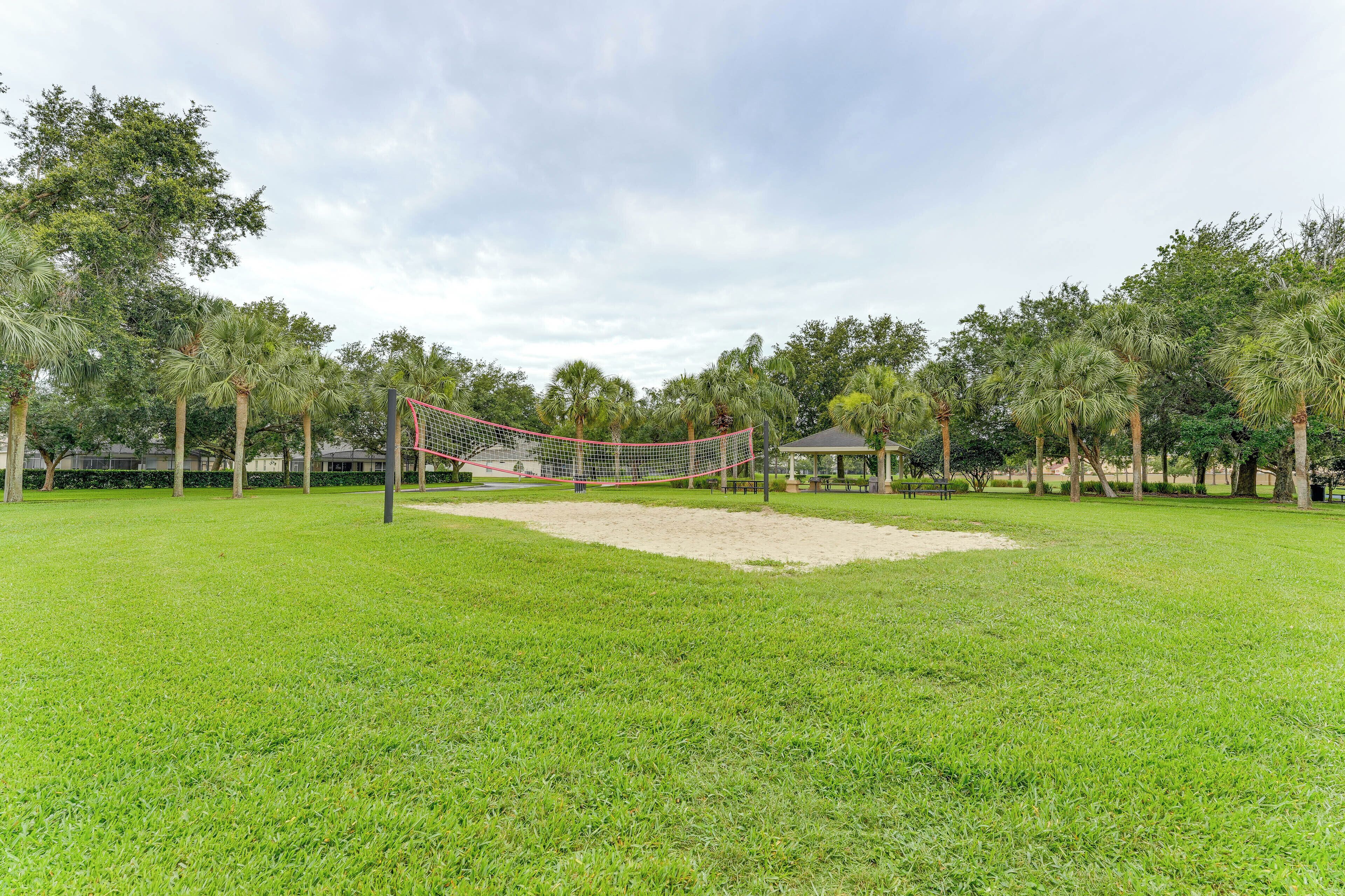 Una cancha de voleibol con red, rodeada de césped verde y árboles.