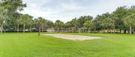 Una cancha de voleibol con red, rodeada de césped verde y árboles.