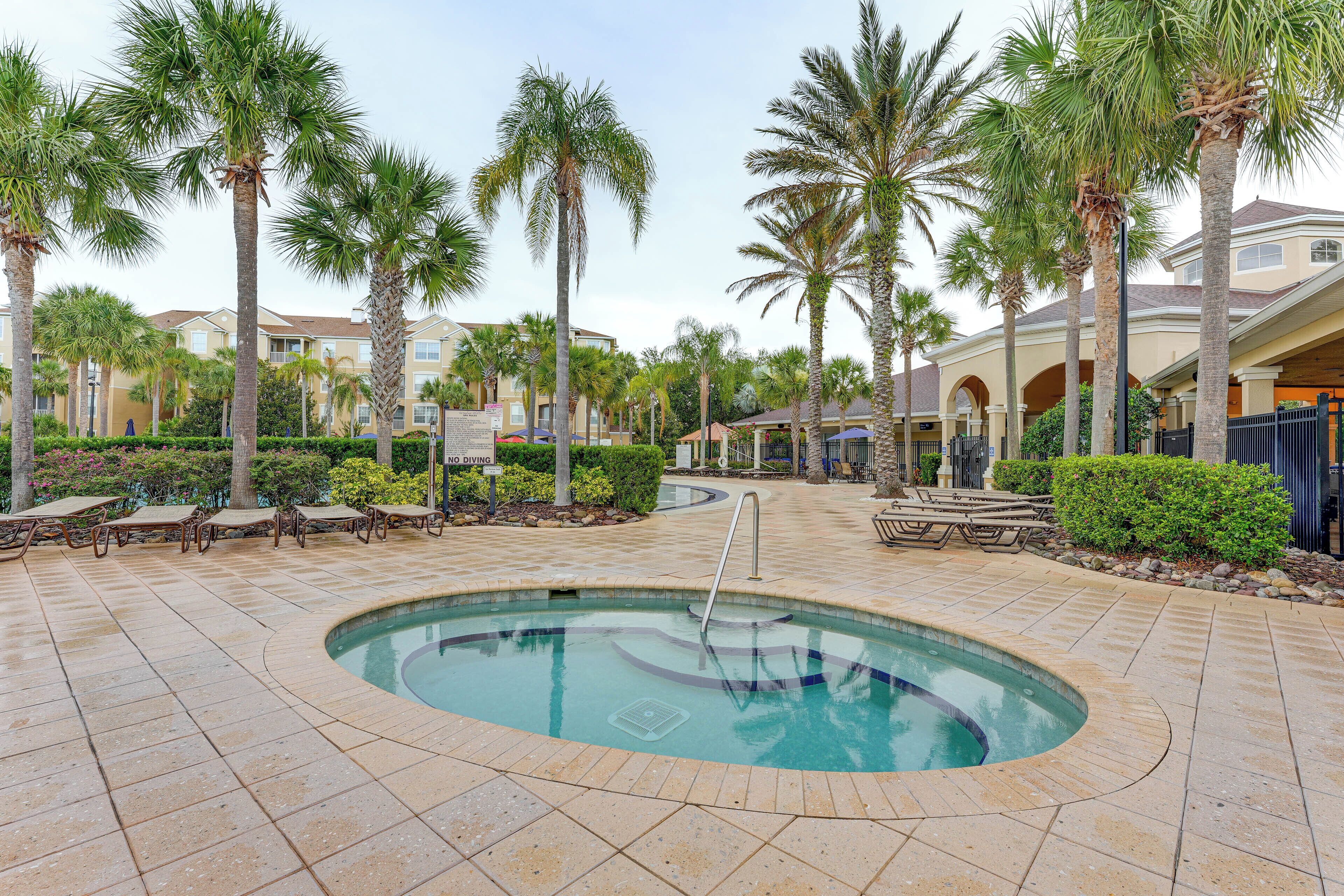 A pool area with palm trees, lounge chairs, and a hot tub.